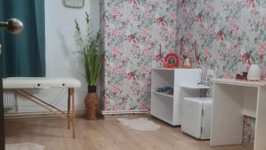A room with a wooden floor, a bench, a potted plant, a wall clock, a shelf with decorative items, and a white cabinet. - Pensiunea Nys (Iasi)
