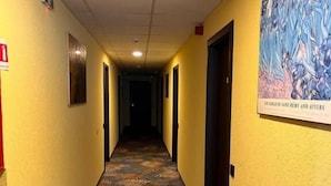 A hotel hallway with patterned carpet, doors, and a painting on the wall. - Pensiunea Nys (Iasi)
