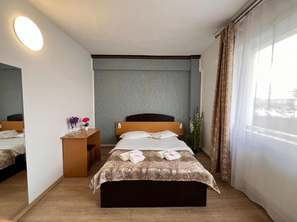 Habitación de hotel con cama, mesita de noche y ventana con cortinas.