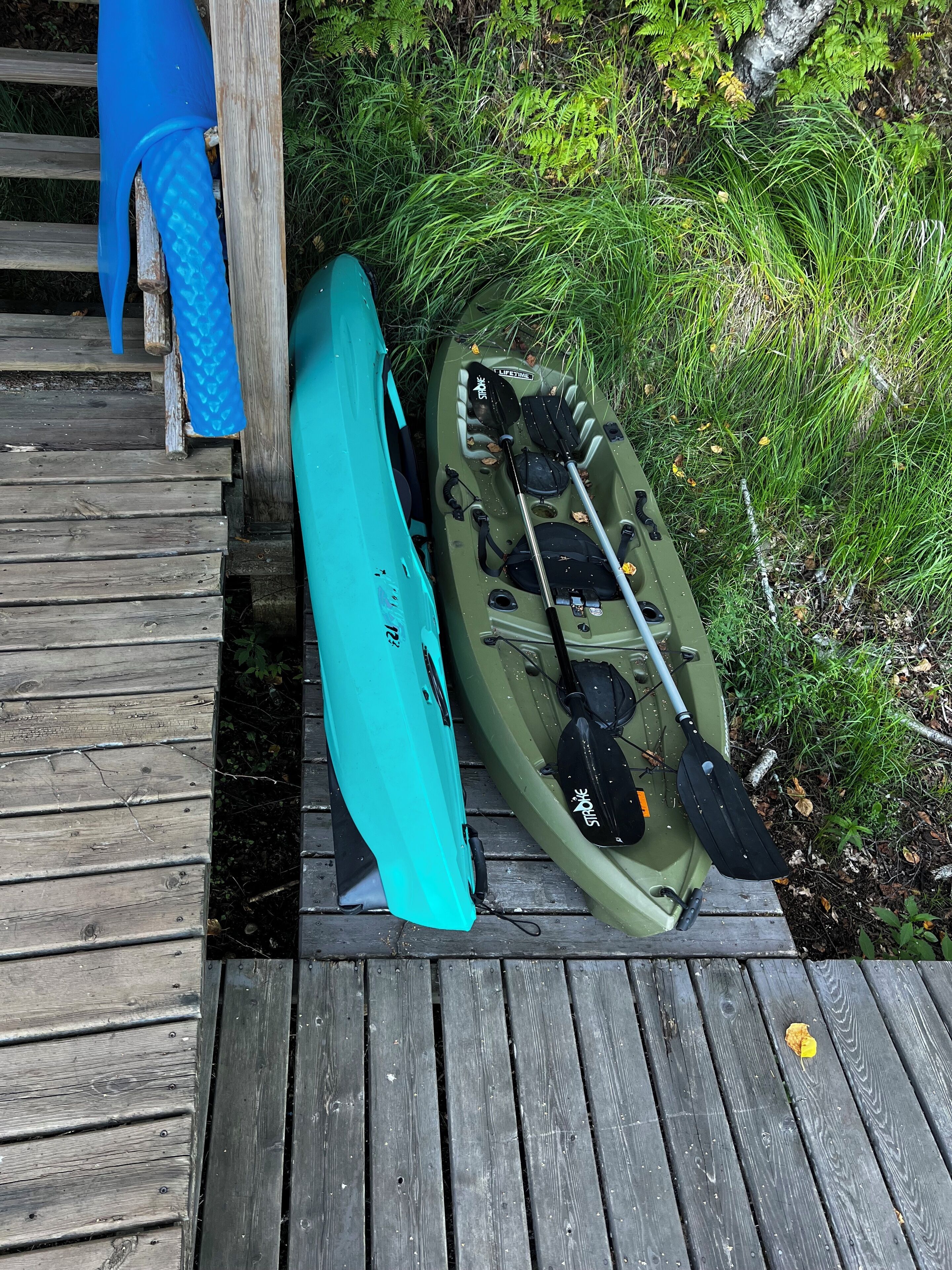 A kayak and paddle leaning against a wooden dock.