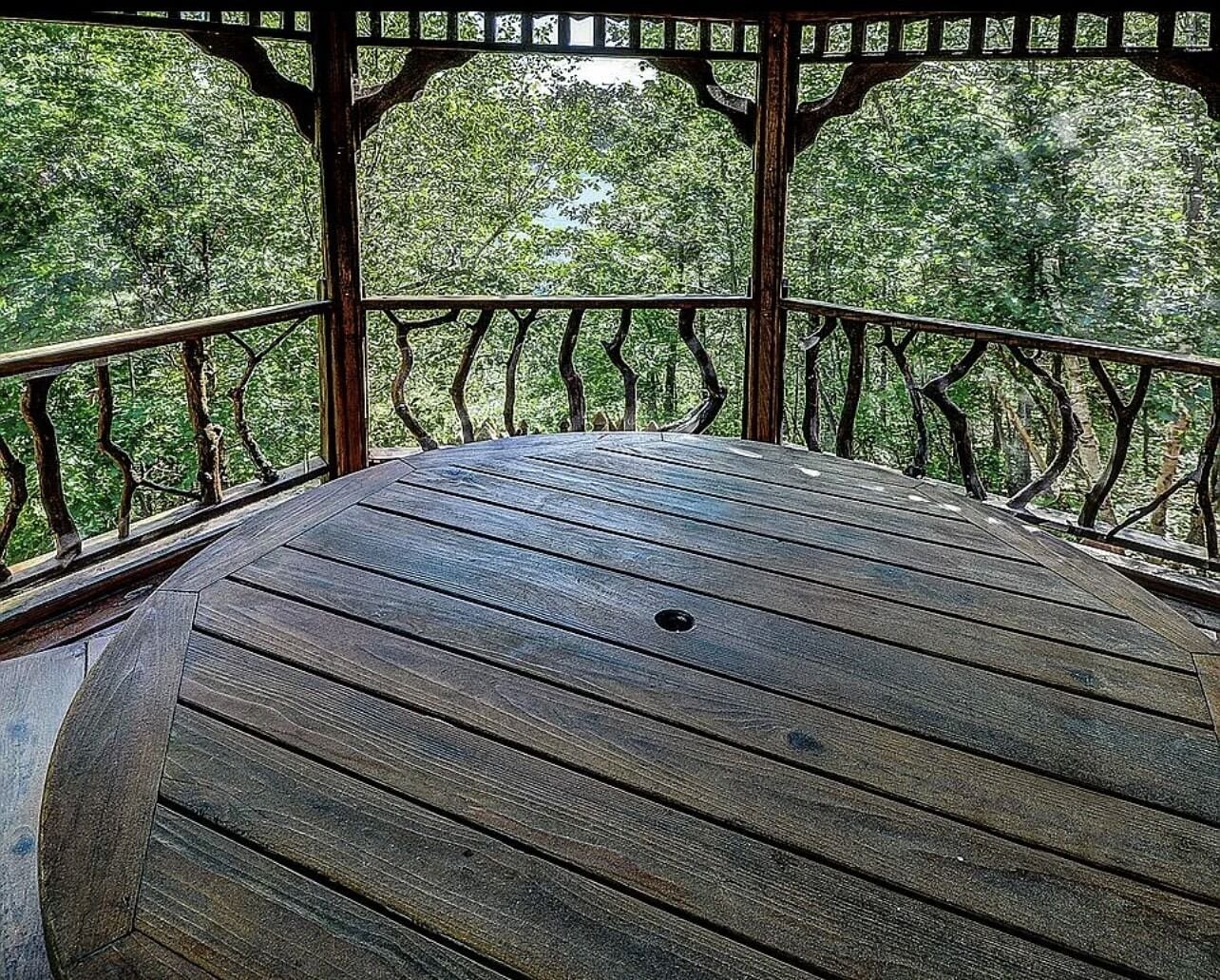 Una terraza de madera con barandilla, rodeada de árboles.