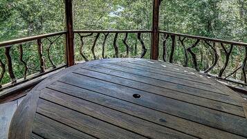 A wooden deck with a railing, surrounded by trees.
