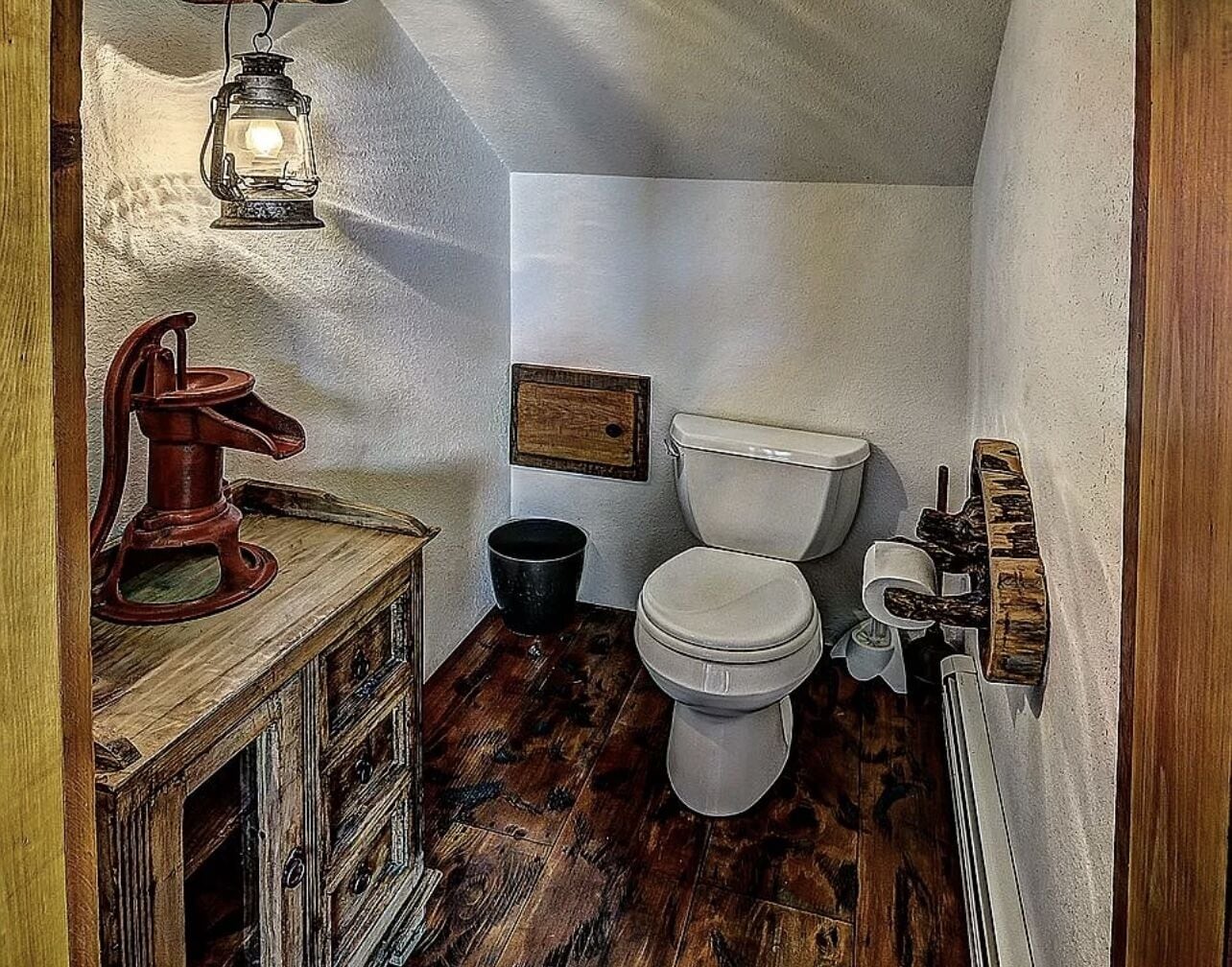 Un bagno compatto con pavimento in legno rustico, un water bianco, un catino di legno e una lanterna d'epoca.