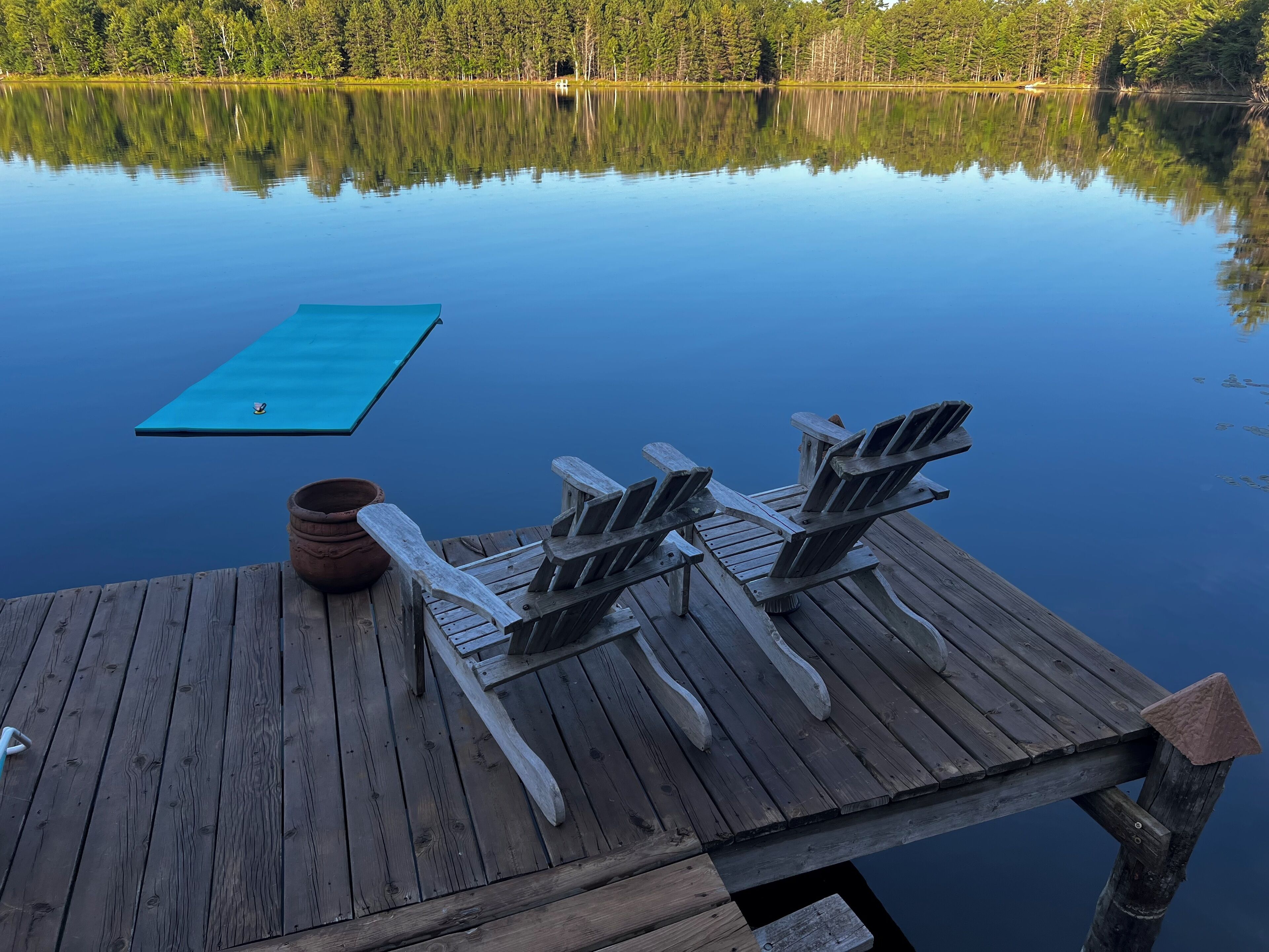 Puinen laituri, jossa on kaksi Adirondack-tyylistä tuolia ja sininen kelluva alusta.