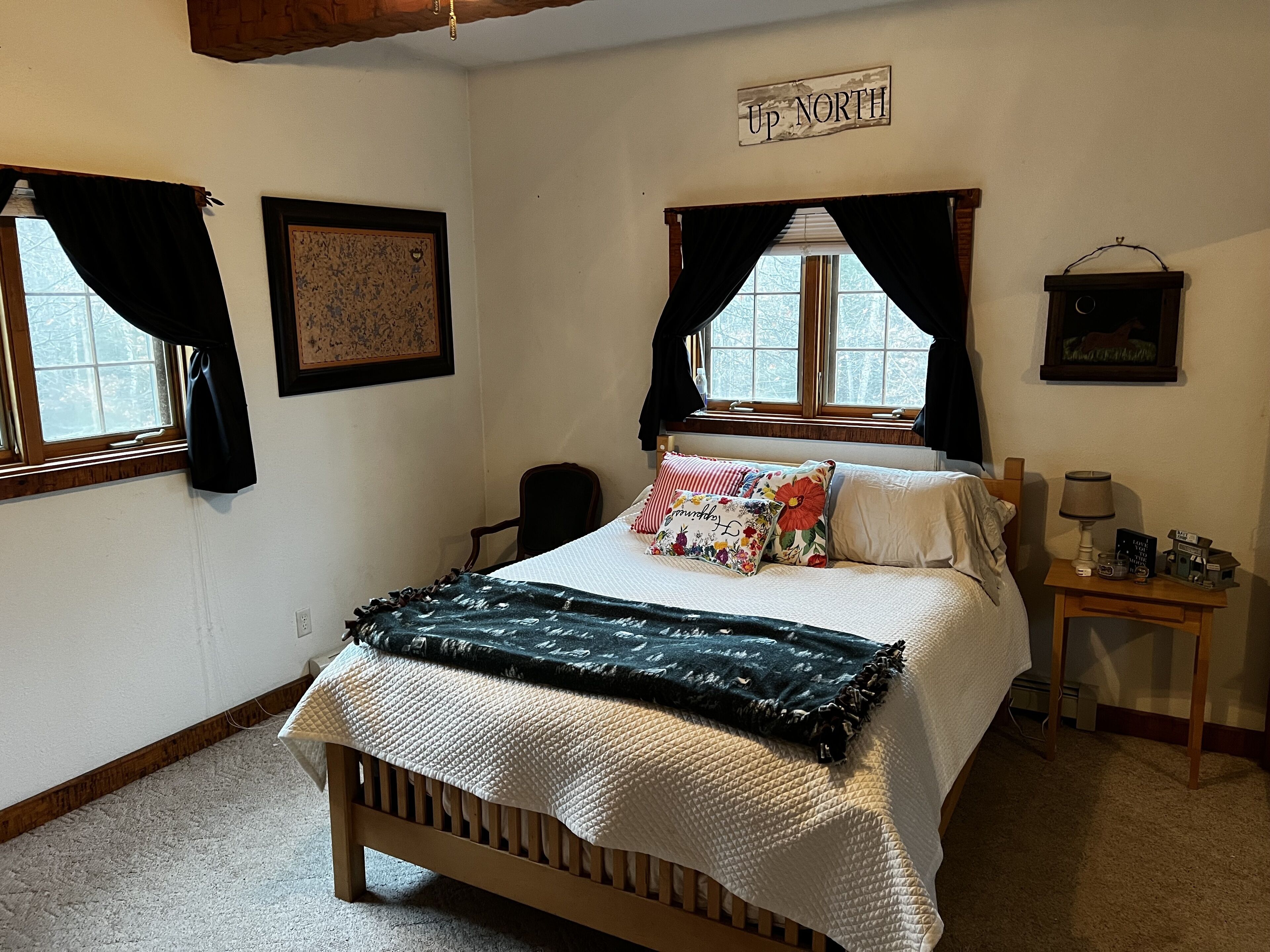 Une chambre à coucher avec un lit, deux fenêtres, une table de chevet et une pancarte sur laquelle on peut lire « Up North ».