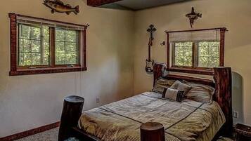 A bedroom with a large bed, two windows, wooden beams, and a ceiling fan.