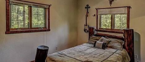 A bedroom with a large bed, two windows, wooden beams, and a ceiling fan.