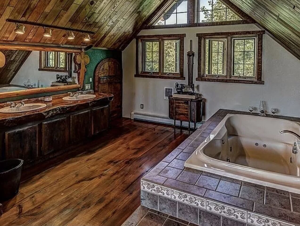A spacious bathroom with a large bathtub, wooden vanity, and multiple windows providing natural light.