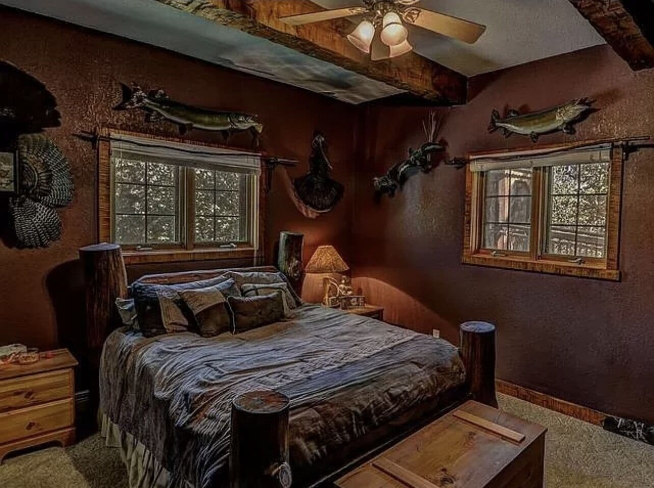 Une chambre avec un grand lit, deux fenêtres, un ventilateur de plafond et des éléments de décoration fixés au mur.