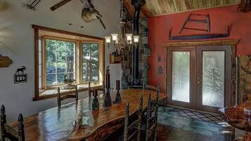 A rustic dining area with a large wooden table, a chandelier, and a stone fireplace.