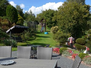 Een tuinpatio met buitenmeubilair, een kinderspeelplaats en een vijver.