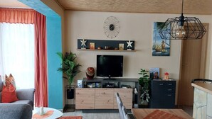 A modern living room with a TV, wooden cabinet, and a dining area with a table and chairs.