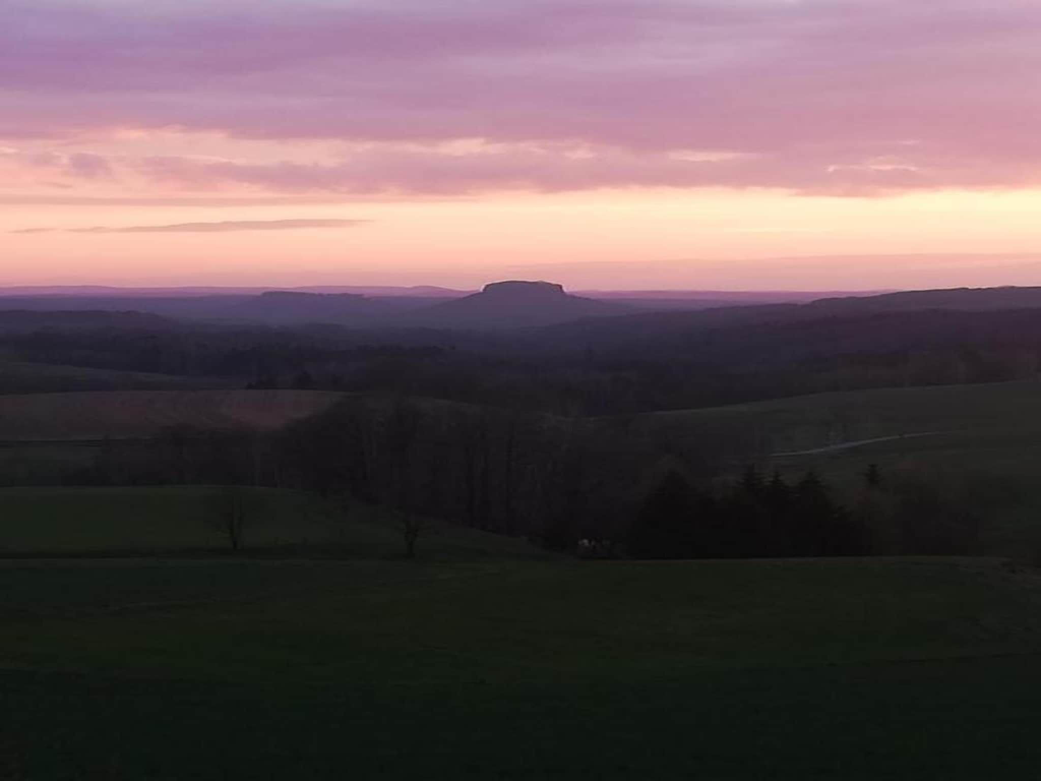 Une vue panoramique d’un paysage vallonné, avec une colline imposante qui se détache à l’horizon.