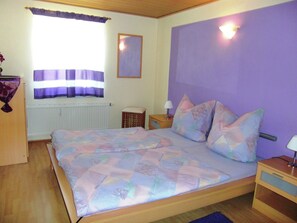 Een slaapkamer met een bed, nachtkastje, lamp, raam met gordijnen en een radiator.