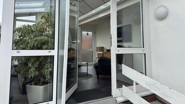 Ein modernes Interieur mit Glastür zu einem Wohnbereich, einer Topfpflanze und einer Treppe.