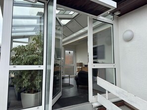 A modern interior with a glass door leading to a living area, a potted plant, and a staircase. - Holiday home Max with fireplace in Thale-Friedrichsbrunn (Thale (OT Friedrichsbrunn))