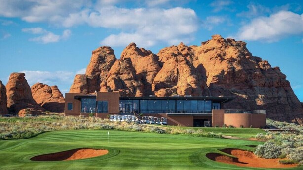 A modern building with large windows, surrounded by a well-maintained golf course and red rock formations. - Desert Jewel In Sand Hollow (Hurricane)