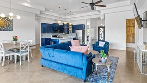 A spacious living area with a blue sofa, dining table, and chairs. A kitchen with blue cabinets and a central island is visible in the background. - Desert Jewel In Sand Hollow (Hurricane)
