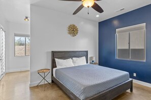 A bedroom with a bed, a ceiling fan, a wall-mounted light fixture, and a window. - Desert Jewel In Sand Hollow (Hurricane)