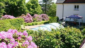 Um jardim com piscina, área de estar coberta e uma casa com telhado inclinado.