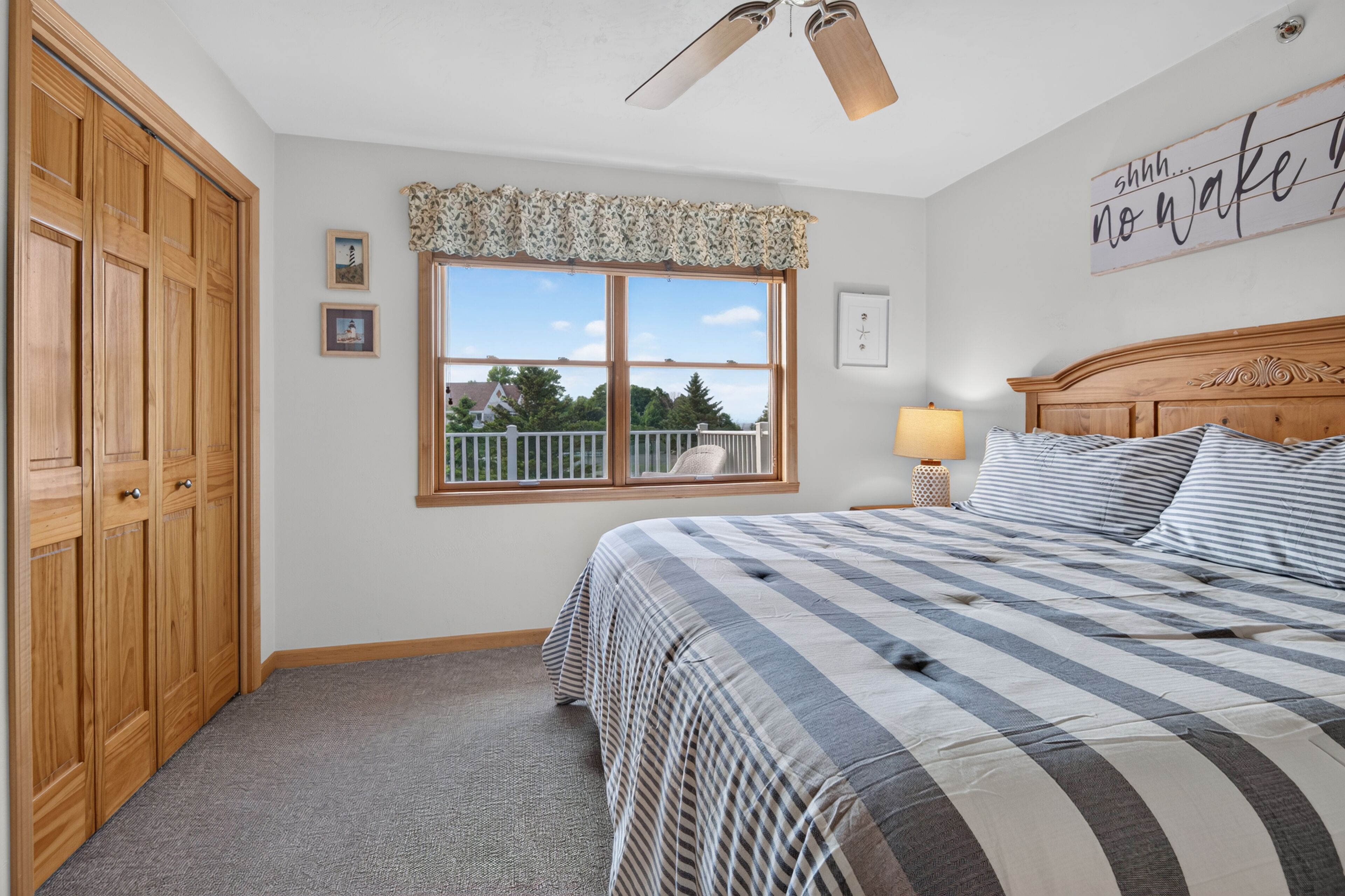 Un dormitorio con cama, ventana con vistas, ventilador de techo y pared con un letrero.