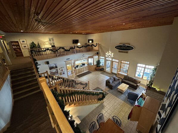 Un hall d’entrée spacieux avec un plafond haut, des poutres en bois, un escalier et un coin salon agrémenté d’une cheminée.