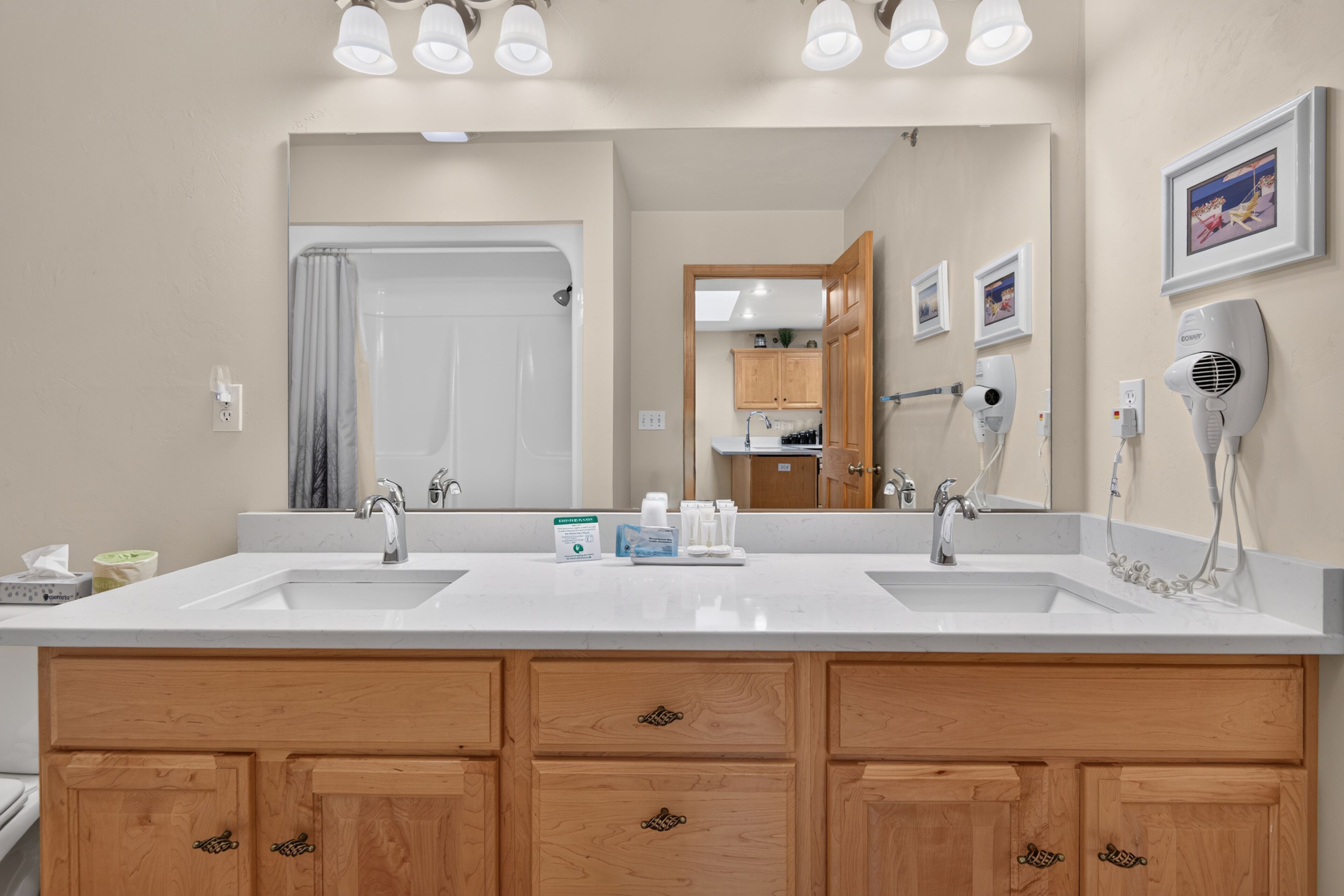 A bathroom with two sinks, wooden cabinets, a large mirror, and a hairdryer.