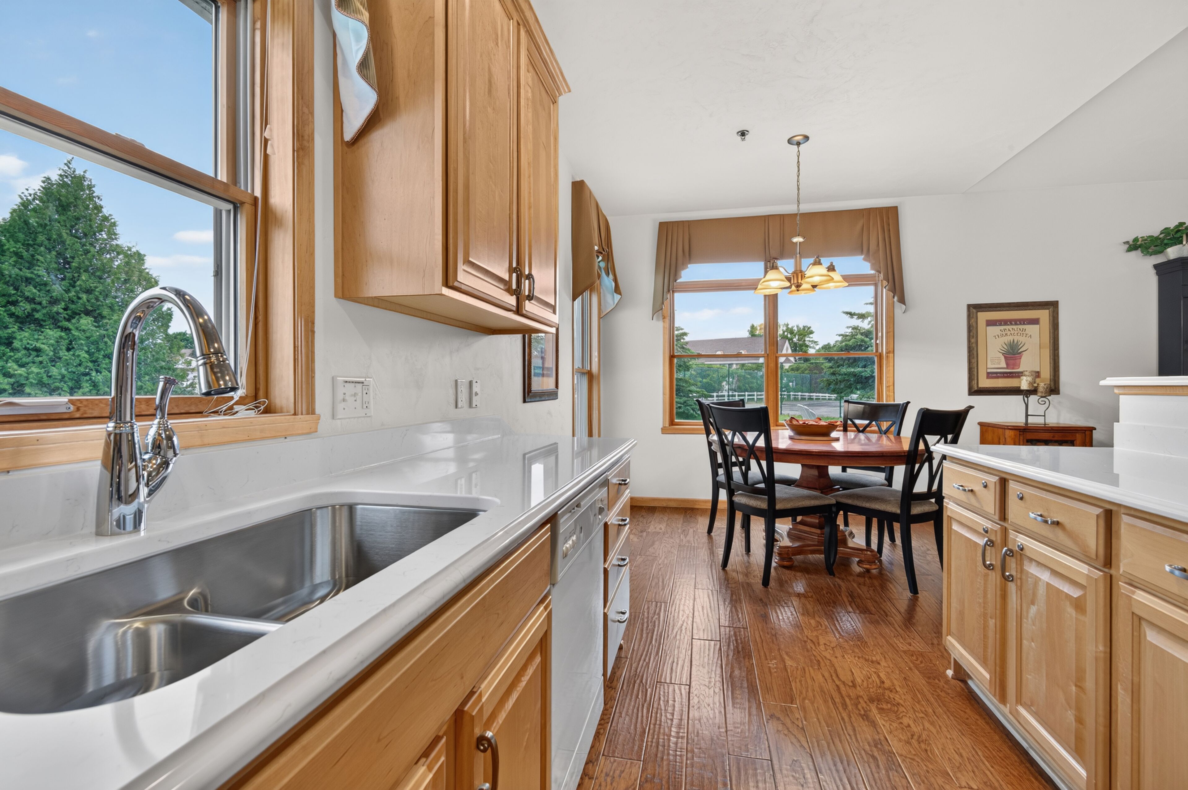 A kitchen with wooden cabinets, a double sink, and a dining area with a table and chairs.