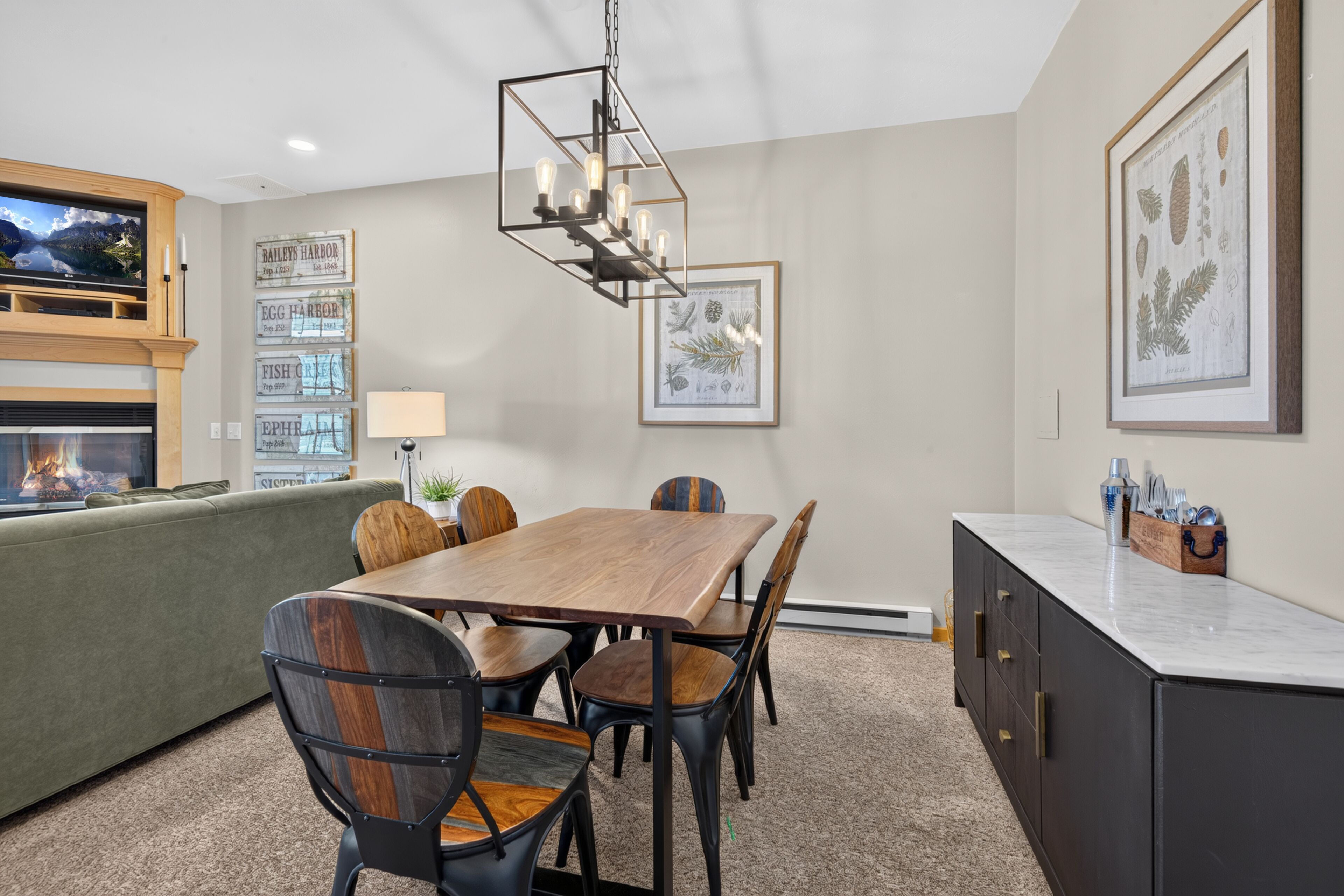A dining area with a wooden table, chairs, a chandelier, and framed botanical prints on the walls.