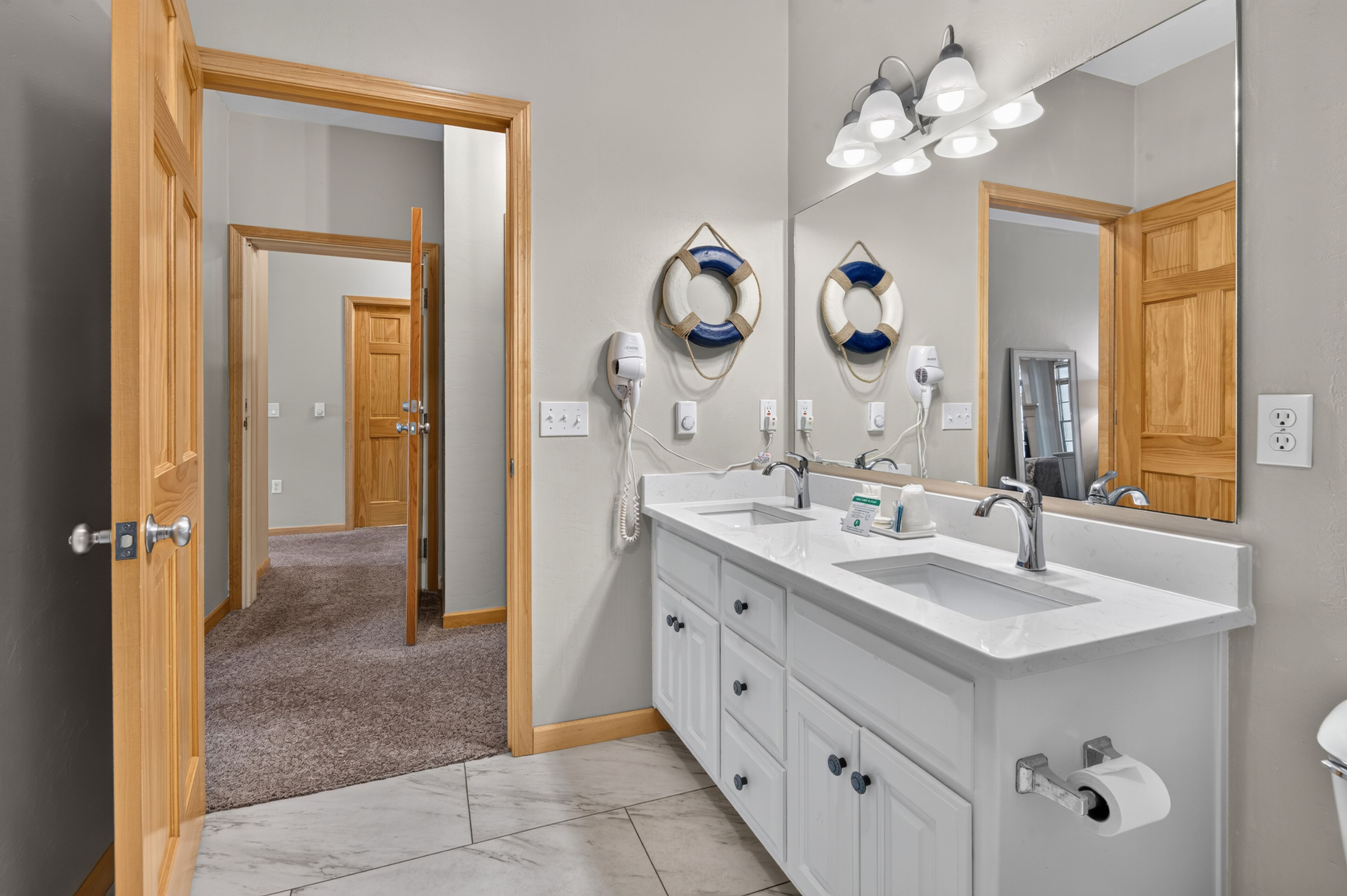 A bathroom with a double sink, wooden cabinetry, a large mirror, and a ceiling light fixture.