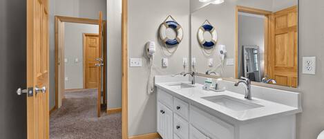 A bathroom with a double sink, wooden cabinetry, a large mirror, and a ceiling light fixture.