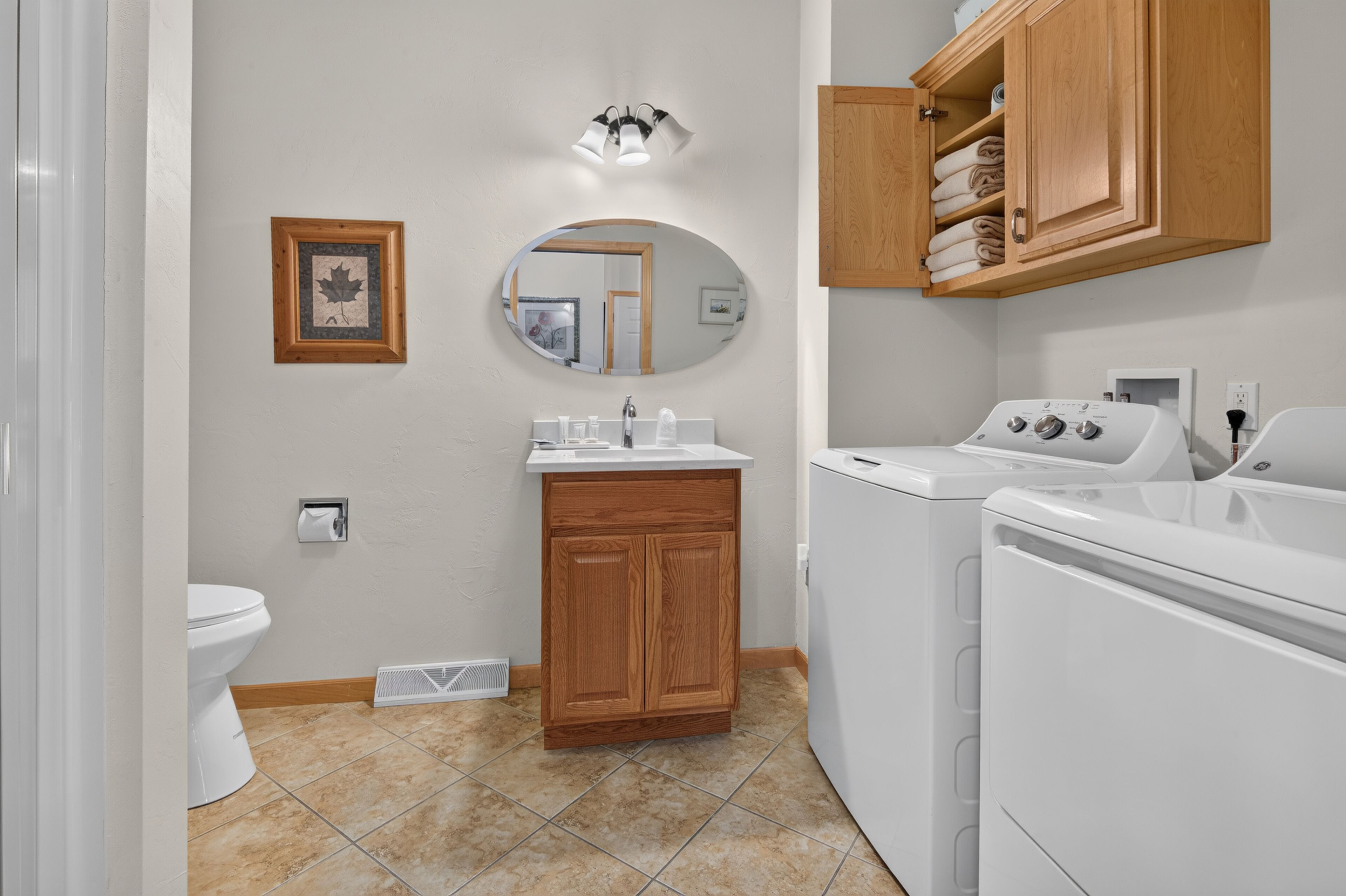 A bathroom with a toilet, sink, mirror, wooden cabinets, and a washing machine.