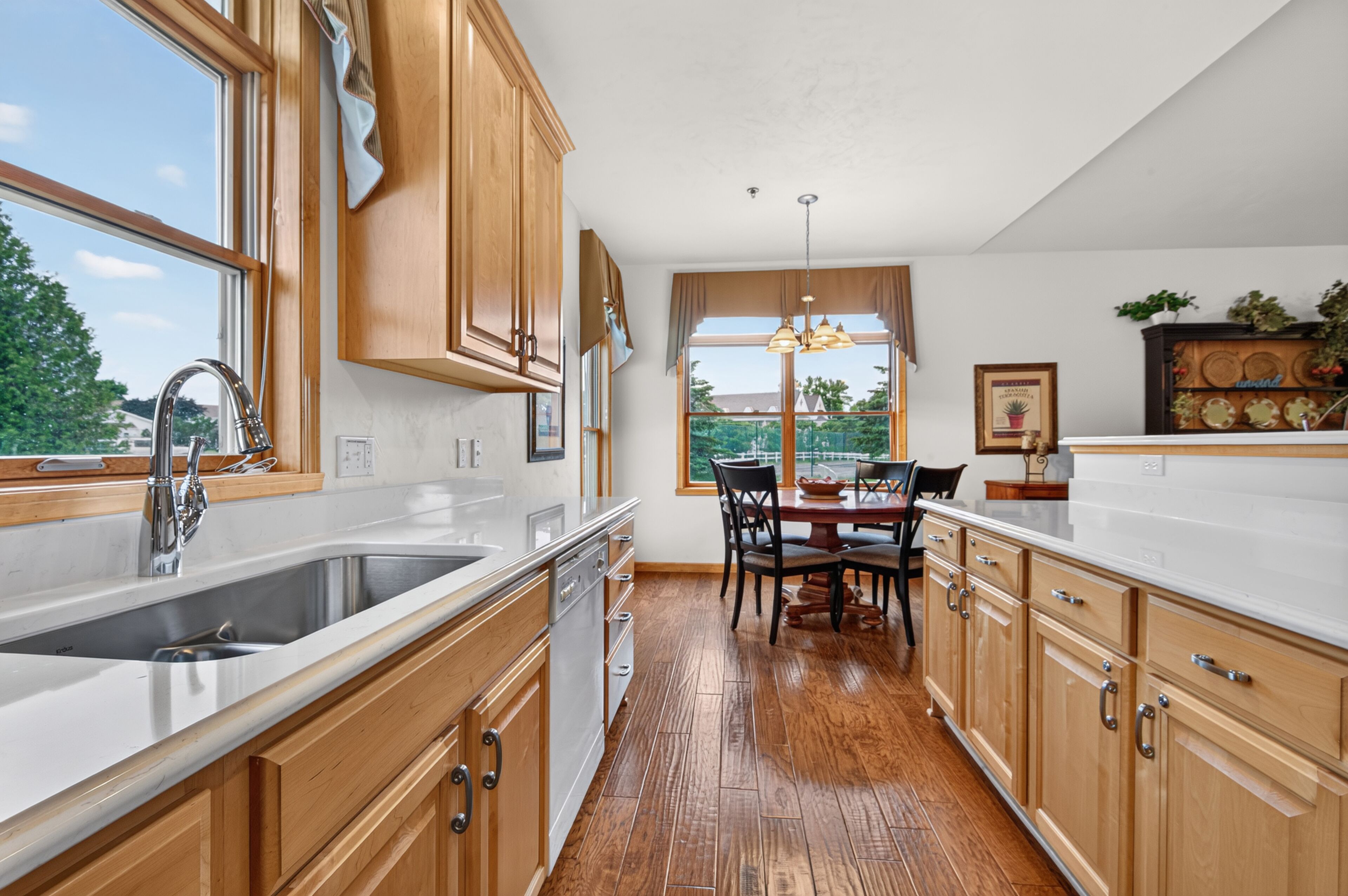 A kitchen with wooden cabinets, a large window, and a dining area with chairs.