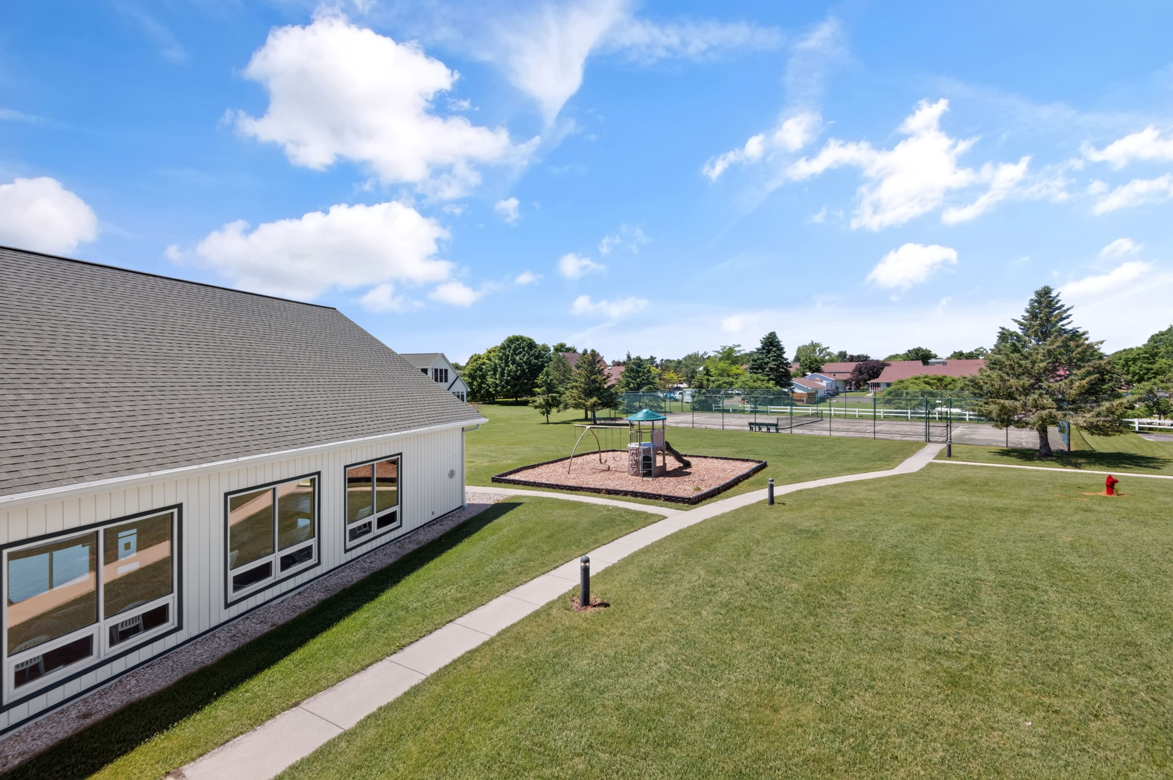 A modern building with large windows, a grassy lawn, and a playground with swings and a slide.