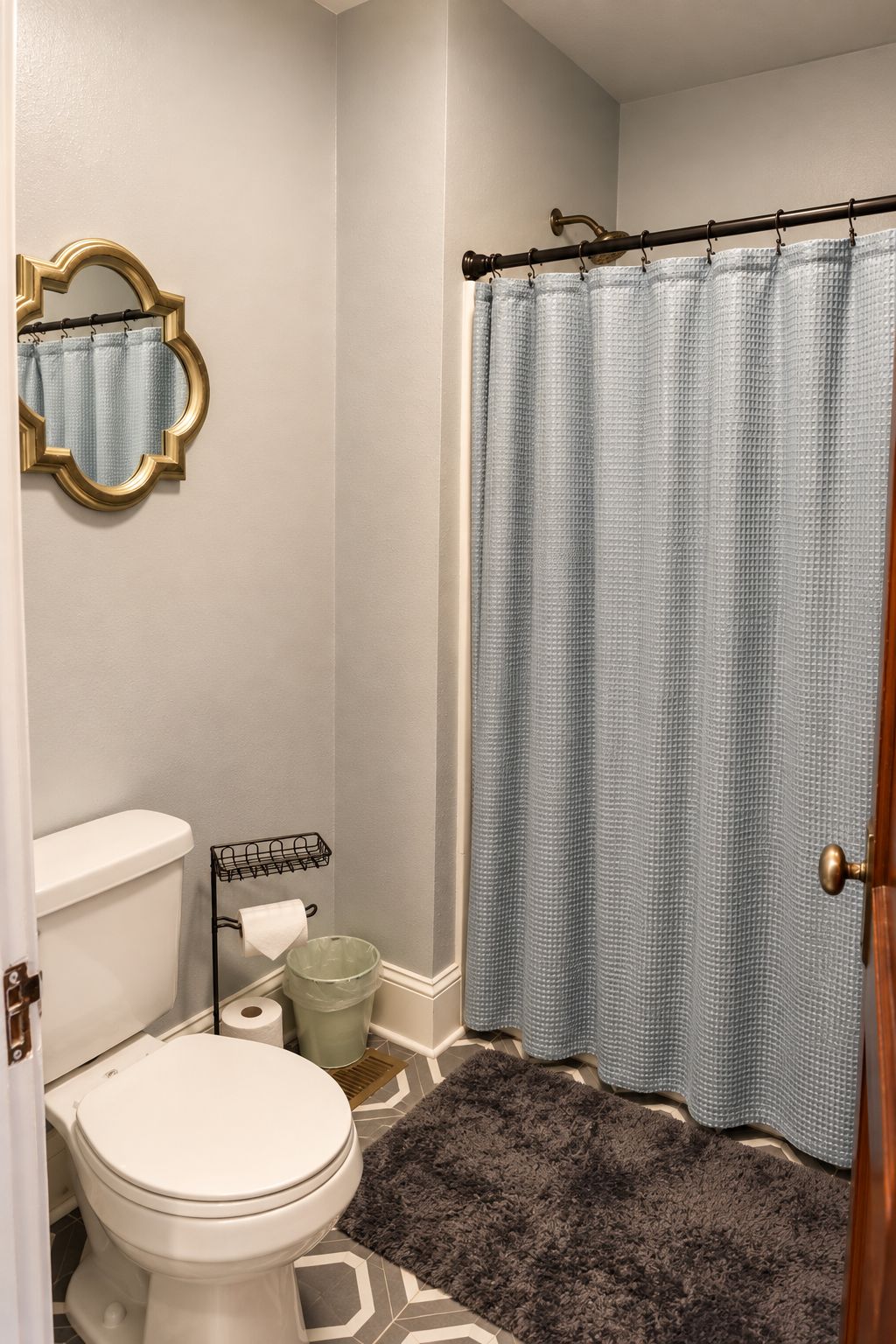 A bathroom with a toilet, a shower curtain, a mirror, and a rug.