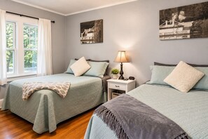A bedroom with two beds, a nightstand, a lamp, and a window with curtains.