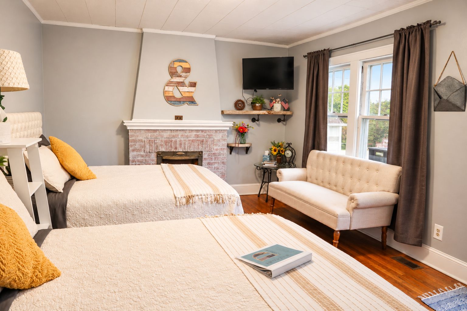 A bedroom with two beds, a fireplace, a television, and a sofa.