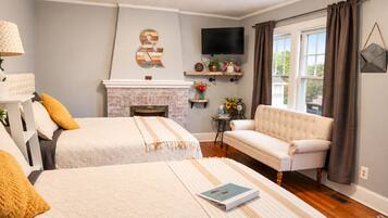 A bedroom with two beds, a fireplace, a television, and a sofa.