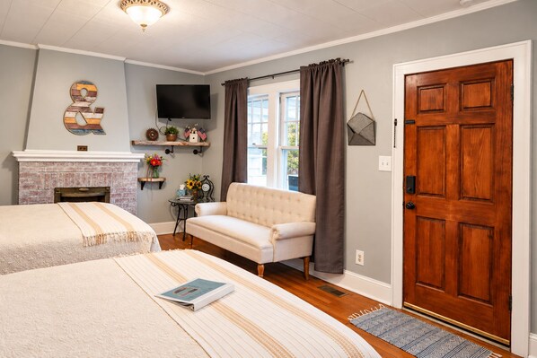 A hotel room with two beds, a fireplace, a television, and a large wooden door.