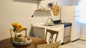 A dining area with a wooden table and chairs, a kitchen with a stove and refrigerator, and a shelf with kitchen items. - Cozy hideaway on Main, Farmhouse Unit (Deadwood)