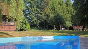 A swimming pool with a clear blue water surface, surrounded by trees and a brick building. - Ferienhaus in Kirchdorf mit Reiterhof (Kirchdorf)