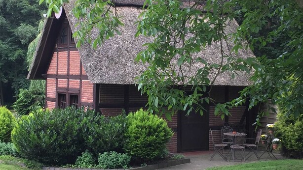 A traditional building with a thatched roof, surrounded by well-maintained greenery and a paved pathway leading to a seating area. - Ferienhaus in Kirchdorf mit Reiterhof (Kirchdorf)