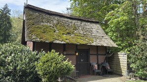 A rustic building with a moss-covered thatched roof, a brick exterior, and a small porch area with outdoor seating. - Ferienhaus in Kirchdorf mit Reiterhof (Kirchdorf)