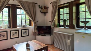 A room with a wooden table, framed pictures, a television, a radiator, and windows with curtains. - Ferienhaus in Kirchdorf mit Reiterhof (Kirchdorf)