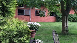 A brick building with a window, a tree, and a metal chair. - Ferienhaus in Kirchdorf mit Reiterhof (Kirchdorf)