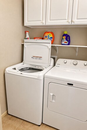 A laundry area with a front-loading washer and dryer, a shelf with cleaning products, and a cabinet above.