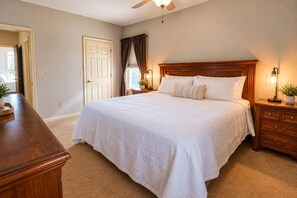 A bedroom with a large bed, wooden headboard, bedside tables with lamps, a nightstand, and a ceiling fan.