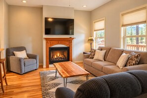 A living room with a fireplace, a sofa, a chair, and a TV mounted on the wall.