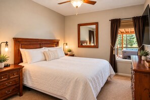 A bedroom with a wooden bed, a nightstand with a lamp, a mirror, and a view of a hot tub outside.