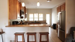 Una cocina moderna con armarios de madera, un refrigerador de acero inoxidable y una barra con taburetes.